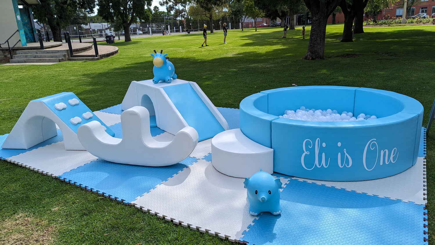 Blue and white soft play set with slide, ball pit, and rocking toy on outdoor grass for toddler event